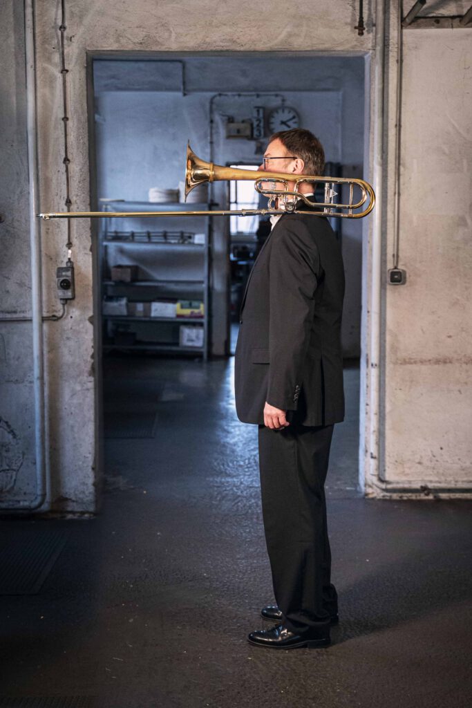 Edgar Manyak Posaunist im Kühnl Trombone Quartet mit Posaune auf der Schulter in der Werkstatt der Blechblasinstrumentenfirma Kühnl & Hoyer in Franken