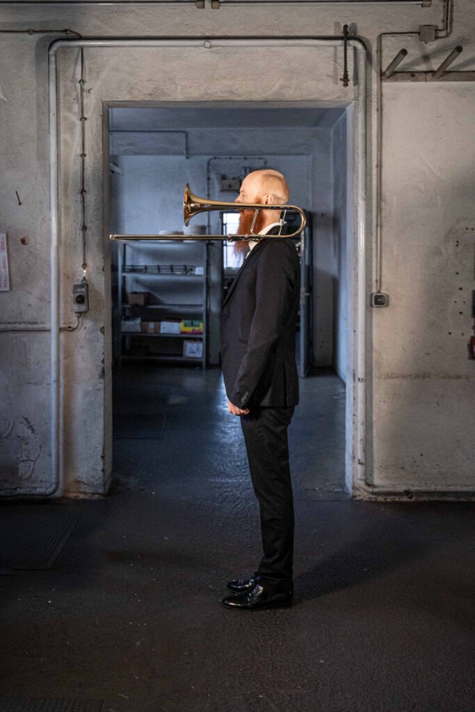Hannes Hölzl Posaunist im Kühnl Trombone Quartet seitlich mit Posaune auf der Schulter in der Werkstatt der Blechblasinstrumentenfirma Kühnl & Hoyer